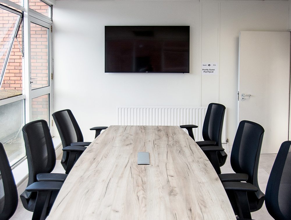 Confererence Table with Mesh Chairs in Front of Wall Mounted TV Screen